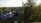 A cozy suburban neighborhood with several houses surrounded by trees. One house features a distinctive blue roof. The area is lush with greenery and bathed in warm evening light, creating a peaceful atmosphere.