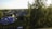 A cozy suburban neighborhood with several houses surrounded by trees. One house features a distinctive blue roof. The area is lush with greenery and bathed in warm evening light, creating a peaceful atmosphere.