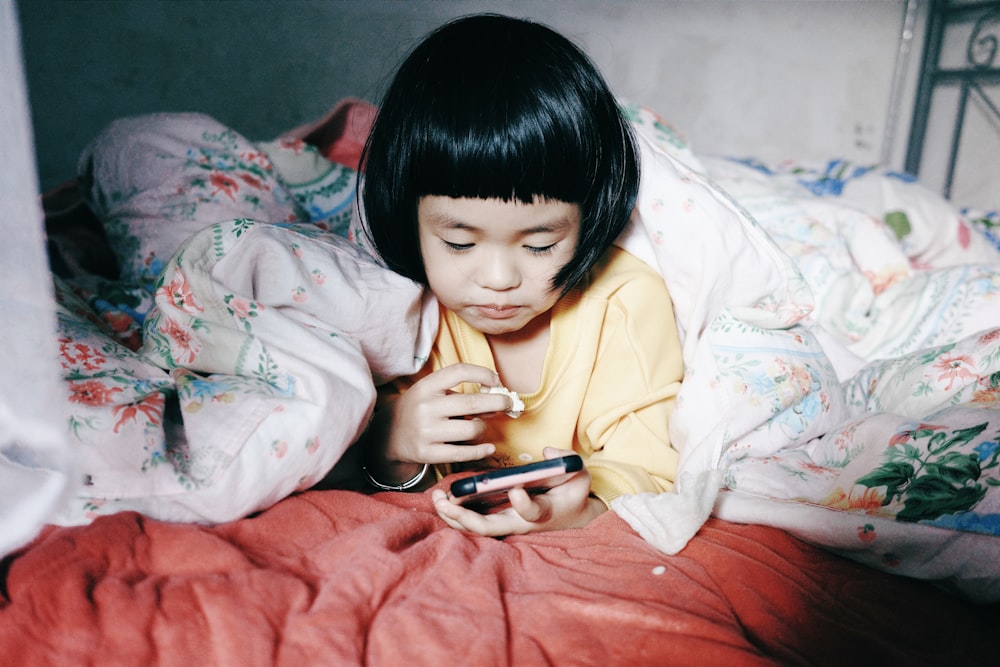 a little girl laying in bed looking at a cell phone
