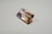 A rectangular, faceted gemstone with a transparent appearance and a gradient of colors ranging from light purple to golden brown. It is placed on a plain, light-colored surface.