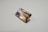 A rectangular, faceted gemstone with a transparent appearance and a gradient of colors ranging from light purple to golden brown. It is placed on a plain, light-colored surface.