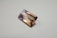 A rectangular, faceted gemstone with a transparent appearance and a gradient of colors ranging from light purple to golden brown. It is placed on a plain, light-colored surface.