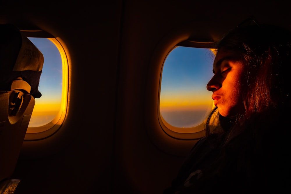 a woman looking out an airplane window at the sunset
