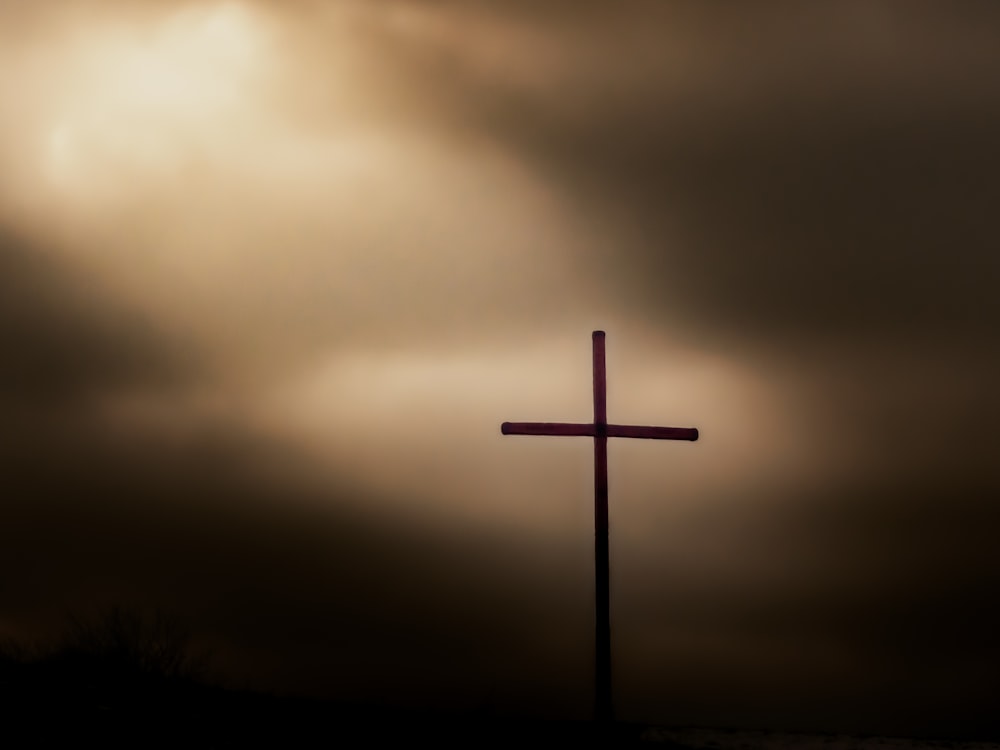 a cross on top of a hill under a cloudy sky