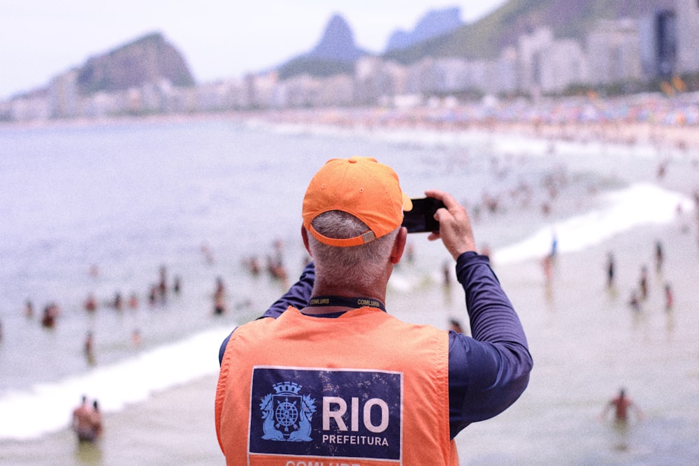 a man in an orange vest is taking a picture of a crowded beach