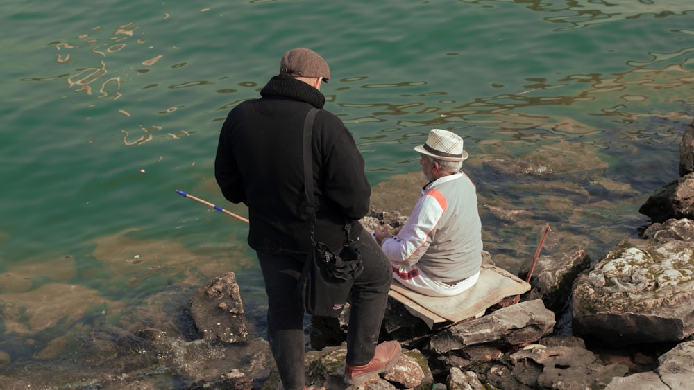 a man and a woman sitting on a rock next to a body of water