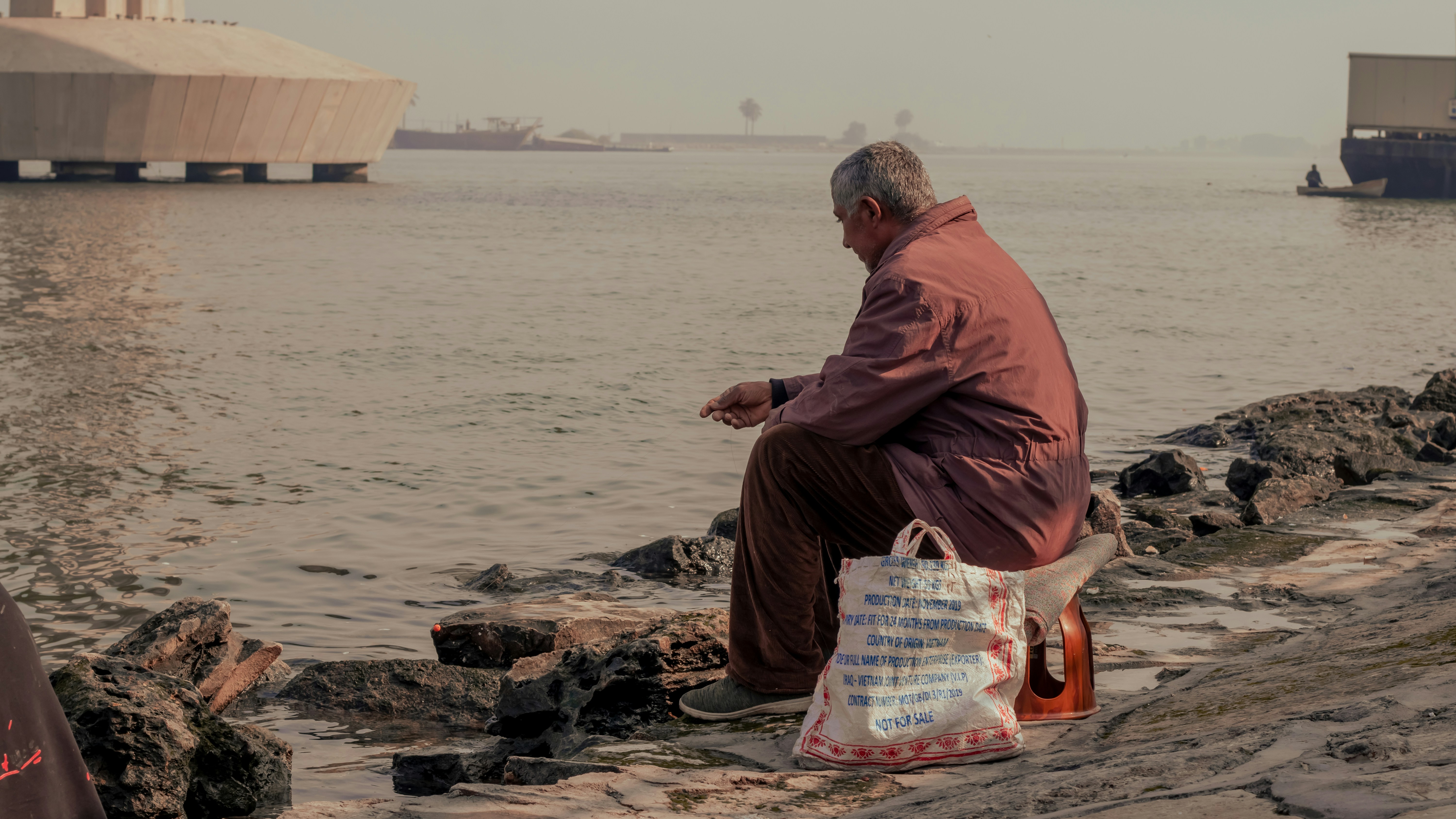 a man sitting on a rock next to a body of water