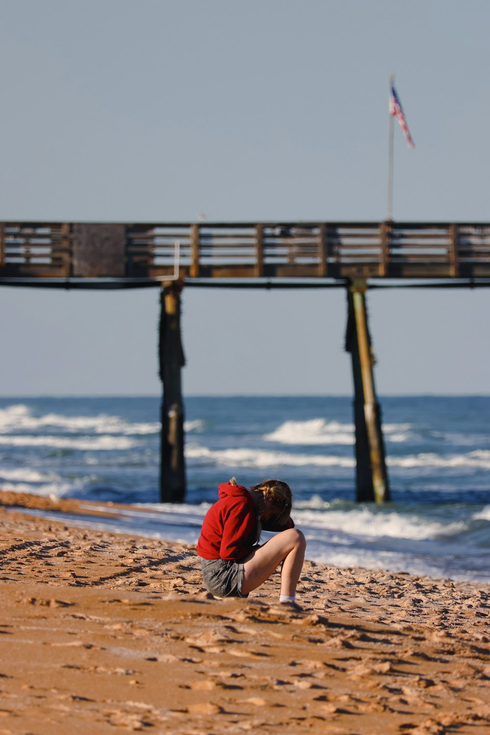um menino sentado na praia olhando para o oceano
