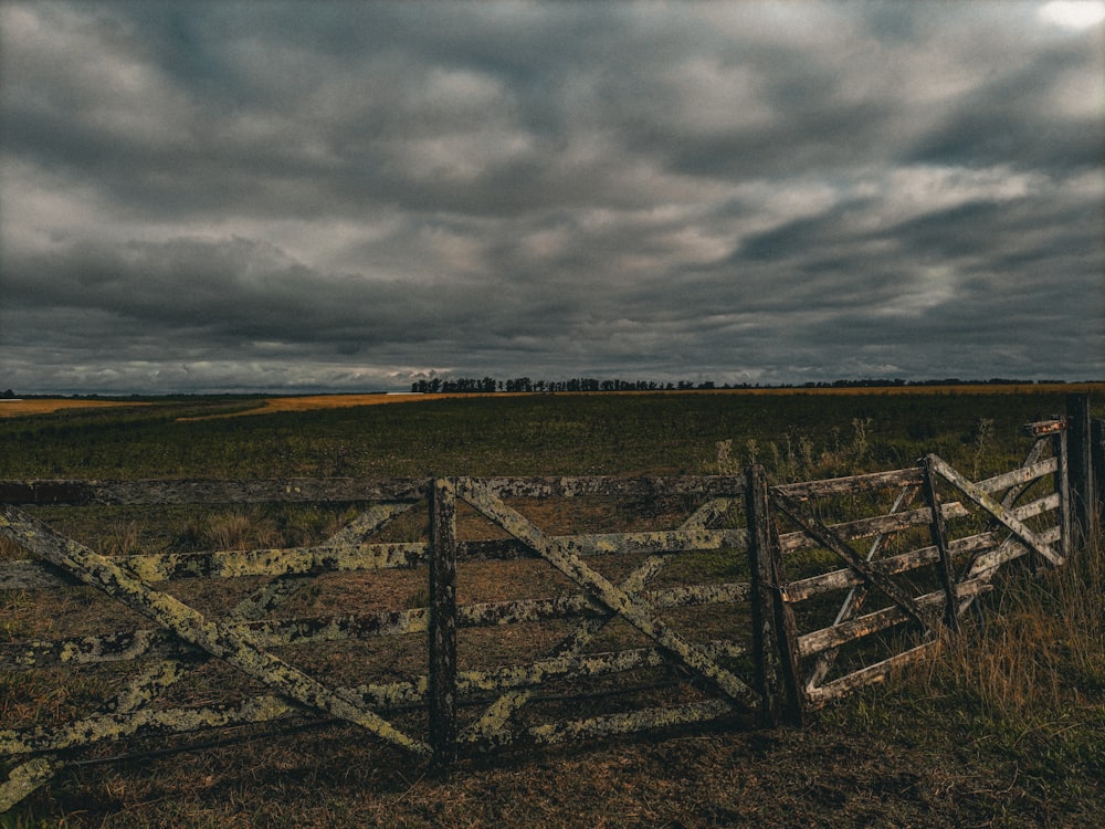 a wooden fence in a grassy field under a cloudy sky