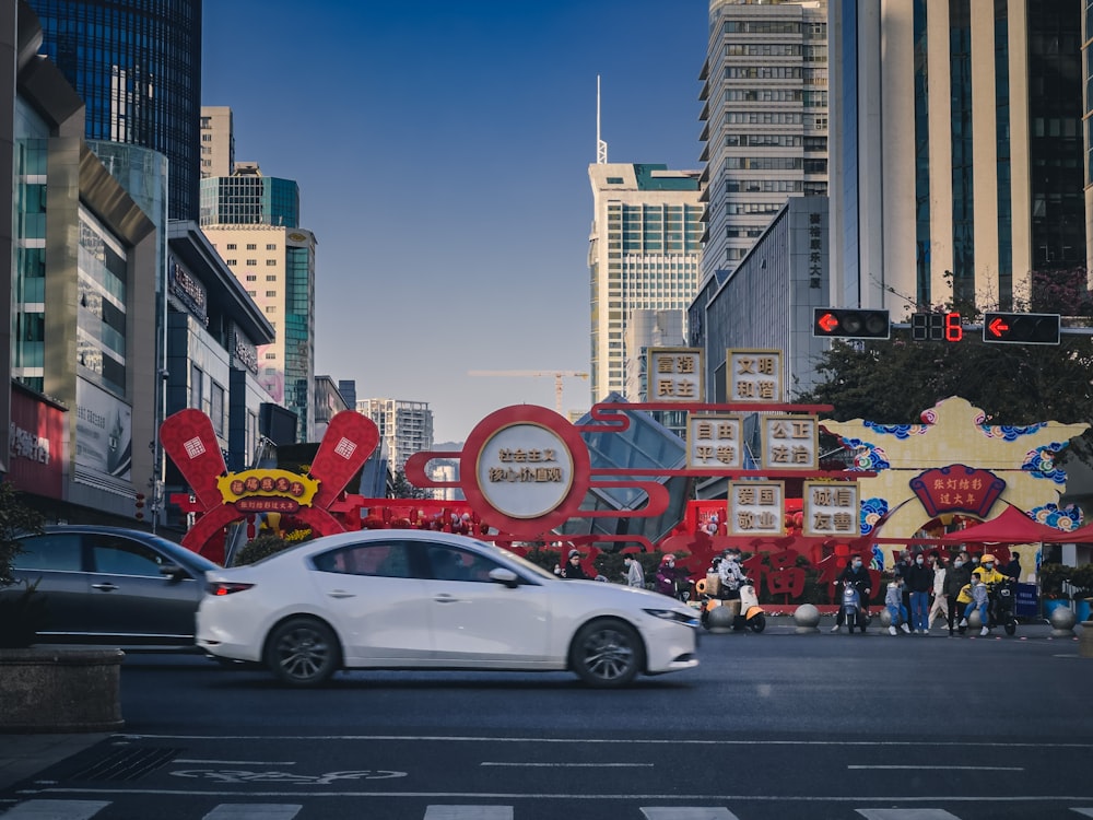 a white car driving down a street next to tall buildings