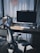A modern home office setup with a sleek desk featuring a large computer monitor, wireless keyboard, and mouse. A comfortable office chair is situated in front of the desk. Books are stacked neatly on the left side. Sunlight streams in through sheer curtains, casting soft shadows across the workspace.