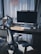 A modern home office setup with a sleek desk featuring a large computer monitor, wireless keyboard, and mouse. A comfortable office chair is situated in front of the desk. Books are stacked neatly on the left side. Sunlight streams in through sheer curtains, casting soft shadows across the workspace.