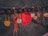 A close-up of a series of love locks hanging on a railing, with focus on a prominent red heart-shaped lock featuring handwritten text. There are several other locks, each with different shapes and colors, including metallic and rustic tones, some tied with strings.