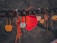 A close-up of a series of love locks hanging on a railing, with focus on a prominent red heart-shaped lock featuring handwritten text. There are several other locks, each with different shapes and colors, including metallic and rustic tones, some tied with strings.