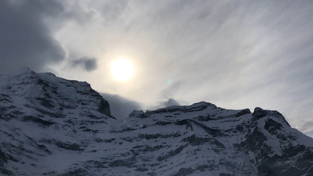 the sun shines through the clouds above a snowy mountain