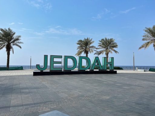 a large sign that says jeddah in front of palm trees