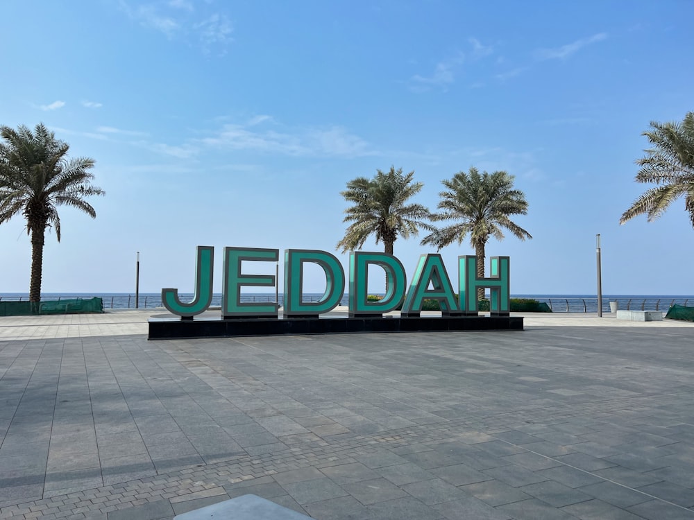 a large sign that says jeddah in front of palm trees
