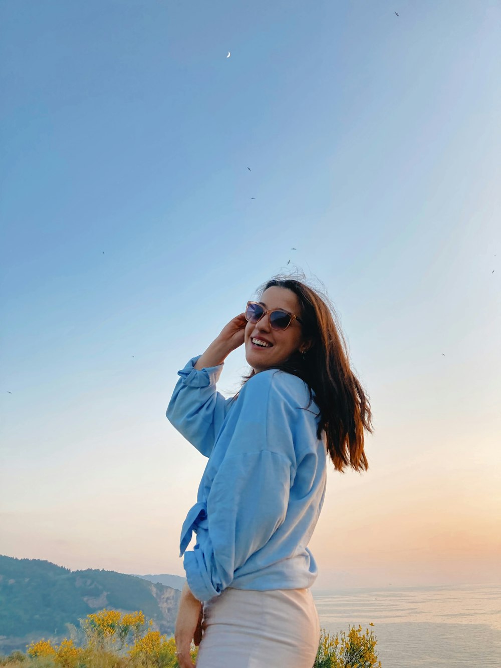 a woman standing on top of a hill near the ocean