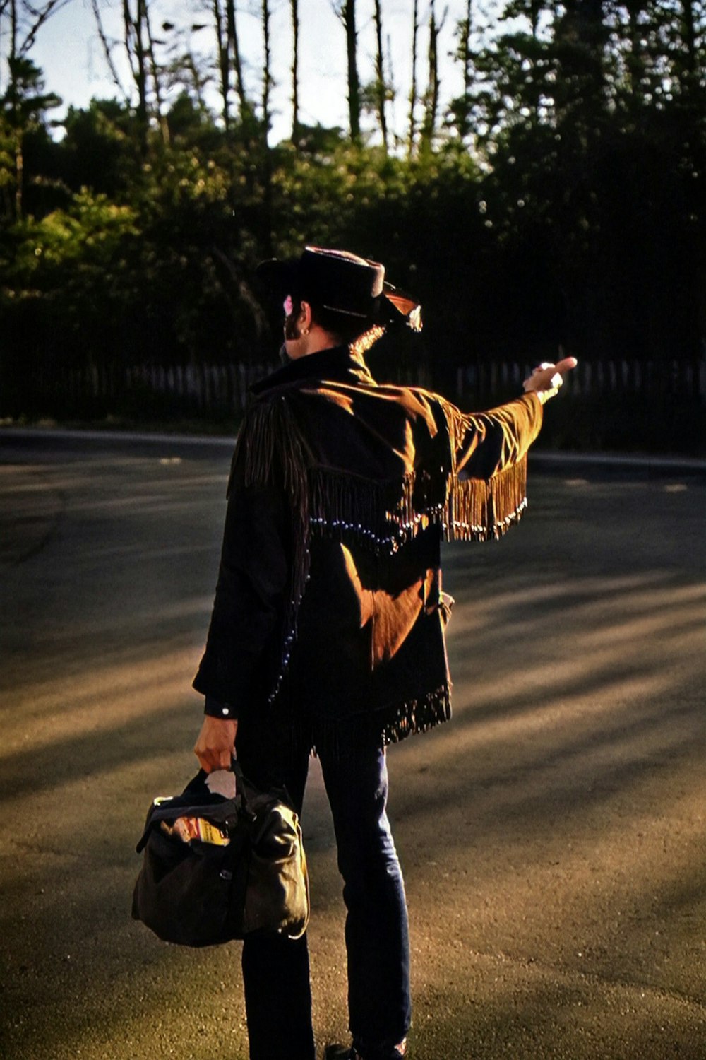 a man standing on the side of a road holding a bag