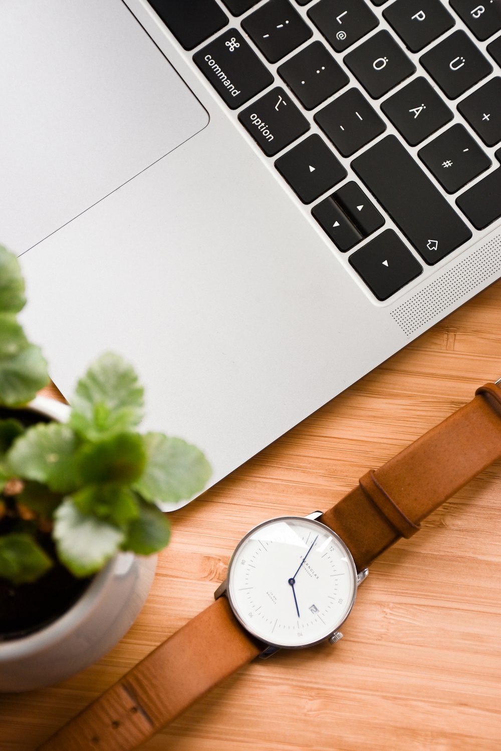 a watch sitting on top of a wooden table next to a laptop