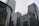 Skyscrapers with glass and steel facades rise against a cloudy sky. Corporate logos like HSBC and Citi are visible on the buildings, indicating major financial institutions. The architecture features modern glass curtain walls and grid patterns.