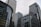 Skyscrapers with glass and steel facades rise against a cloudy sky. Corporate logos like HSBC and Citi are visible on the buildings, indicating major financial institutions. The architecture features modern glass curtain walls and grid patterns.