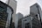 Skyscrapers with glass and steel facades rise against a cloudy sky. Corporate logos like HSBC and Citi are visible on the buildings, indicating major financial institutions. The architecture features modern glass curtain walls and grid patterns.