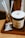 A cup of coffee with a foamy top sits on a wooden tray next to a small glass with paper straws. The cup has a label that reads 'Daily Coffee Service'. Nearby, there is a packaged snack in shiny wrapping.