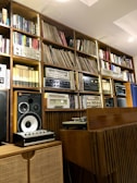 A pair of modern speakers set up on a wooden shelf with vinyl records nearby.