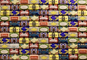 A neatly arranged collection of colorful soap bars, each with unique vintage packaging designs featuring flowers, geometric patterns, and various brand names. The soaps are stacked in rows, creating a visually appealing mosaic-like pattern with a retro aesthetic.