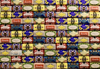 A neatly arranged collection of colorful soap bars, each with unique vintage packaging designs featuring flowers, geometric patterns, and various brand names. The soaps are stacked in rows, creating a visually appealing mosaic-like pattern with a retro aesthetic.