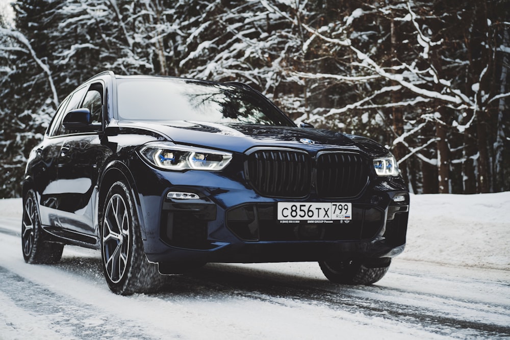 a black bmw suv driving down a snowy road