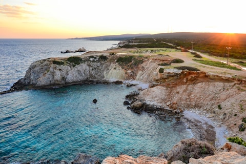 the sun is setting over the water near a rocky shore