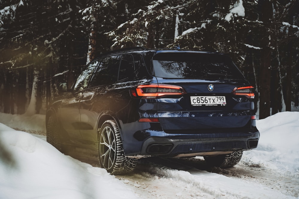 a blue bmw suv driving down a snow covered road