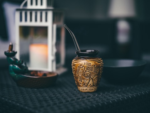 a small gold vase sitting on top of a table next to a candle