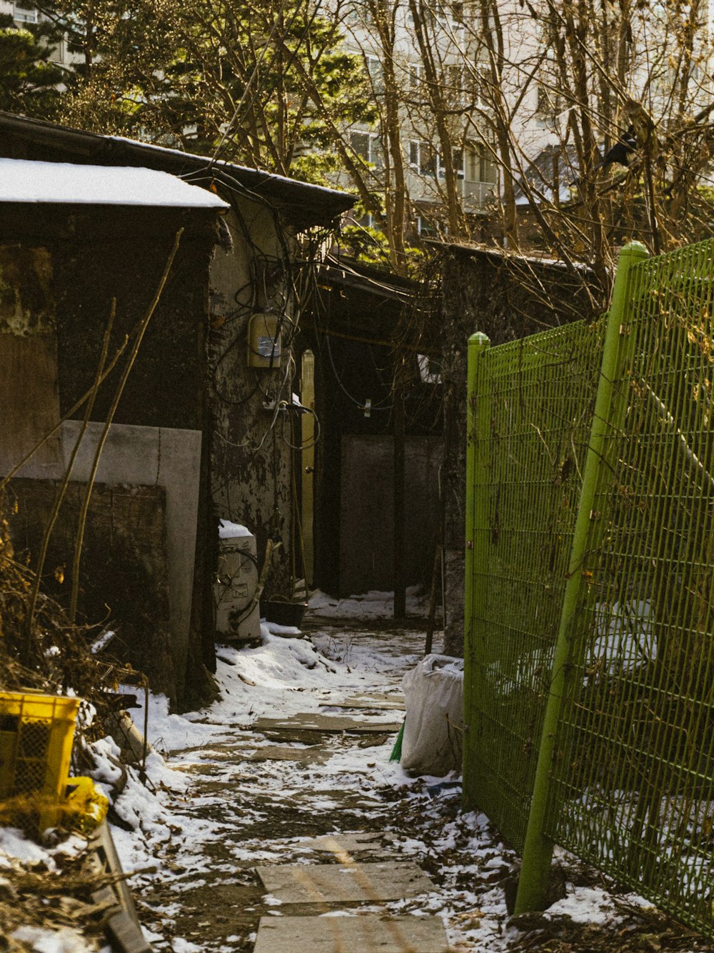 a narrow alley with a green fence and snow on the ground