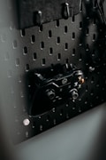 A black gaming controller is mounted on a perforated metal board, with hooks and a headset also visible. The environment appears organized and functional, with a modern aesthetic.