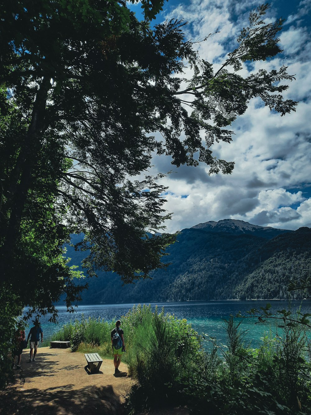 a couple of people walking down a dirt road next to a lake