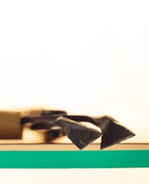 A close-up of sharp metal tools lying on a wooden surface with a striking green stripe across the surface. The background is softly blurred, giving it a bright, minimalistic appearance.