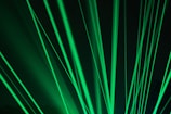 Bright green laser beams shining through a dark background and creating a dynamic, energetic pattern.
