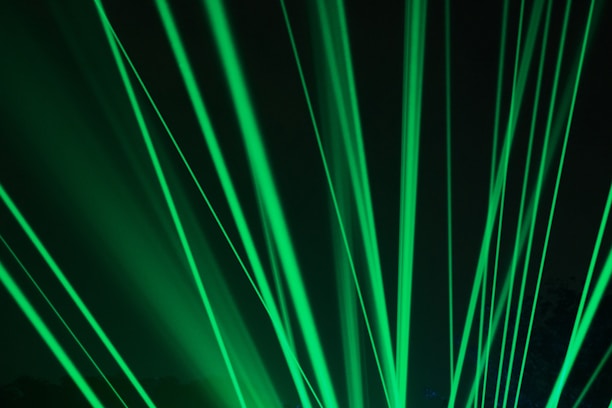 Bright green laser beams shining through a dark background and creating a dynamic, energetic pattern.