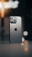 A smartphone with a sleek metallic design is positioned against a blurred background. The device features a triple camera setup and a prominent logo. Ambient lighting casts a warm tone with visible bokeh effects.