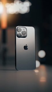 A smartphone with a sleek metallic design is positioned against a blurred background. The device features a triple camera setup and a prominent logo. Ambient lighting casts a warm tone with visible bokeh effects.