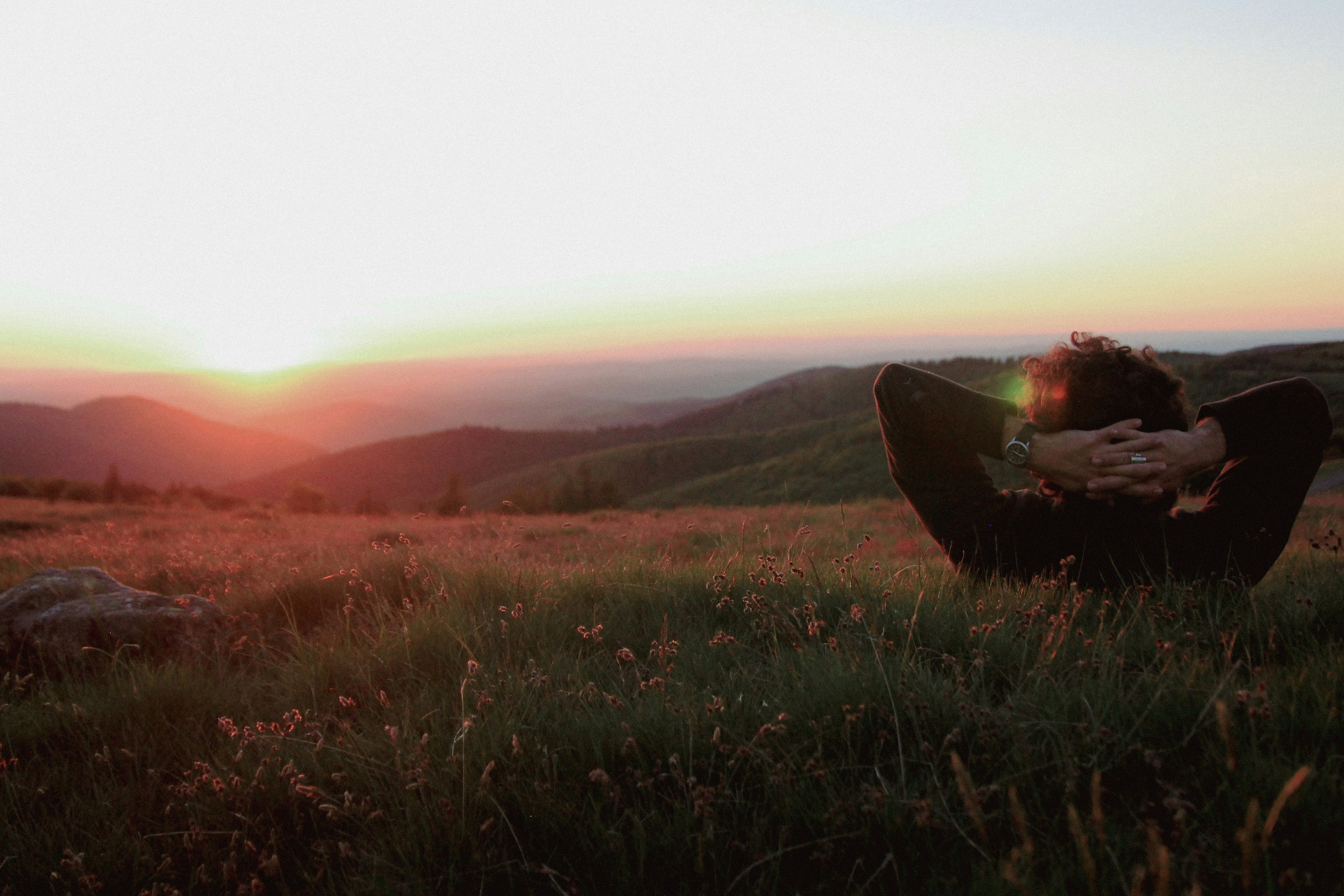 A person sitting in a field with a sunset in the background photo ...