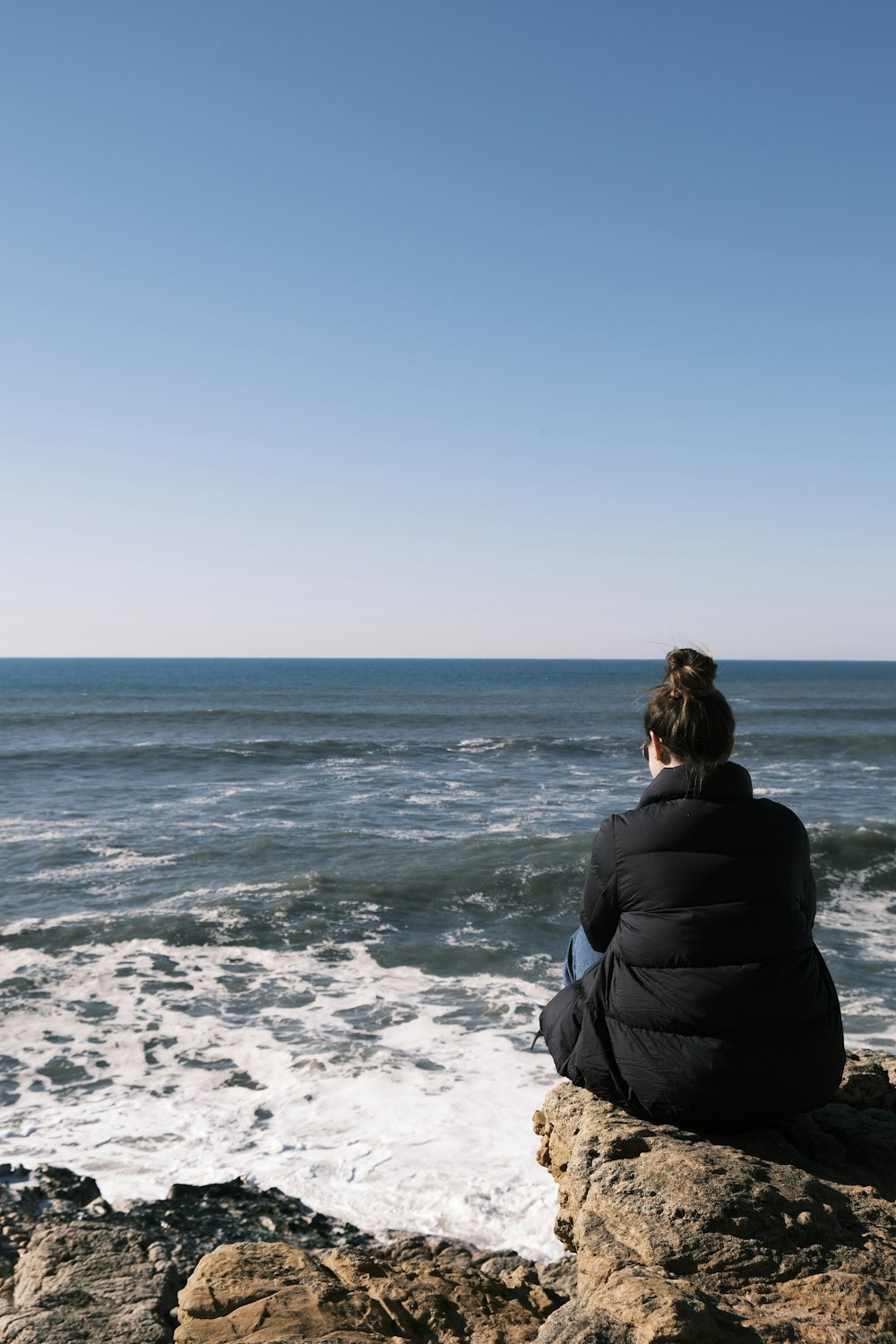 a person sitting on a rock looking out at the ocean