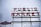 A large sign with the words 'PUBLIC MARKET' in bold red neon letters, supported by a metal framework. To the left, there is an additional sign shaped like a fish with the text 'CITY FISH MARKET'. The background is a cloudy sky, adding a moody atmosphere to the scene.