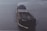 A large cargo ship is sailing on open water. The ship has a dark hull with visible markings and appears to be carrying a large number of shipping containers on its deck. The water around the ship is calm, reflecting the light of the overcast sky.