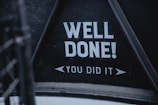 Bold white text on a black background reads 'WELL DONE! YOU DID IT'. The text is framed within a triangular section, suggesting a sign or message board.