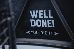 Bold white text on a black background reads 'WELL DONE! YOU DID IT'. The text is framed within a triangular section, suggesting a sign or message board.