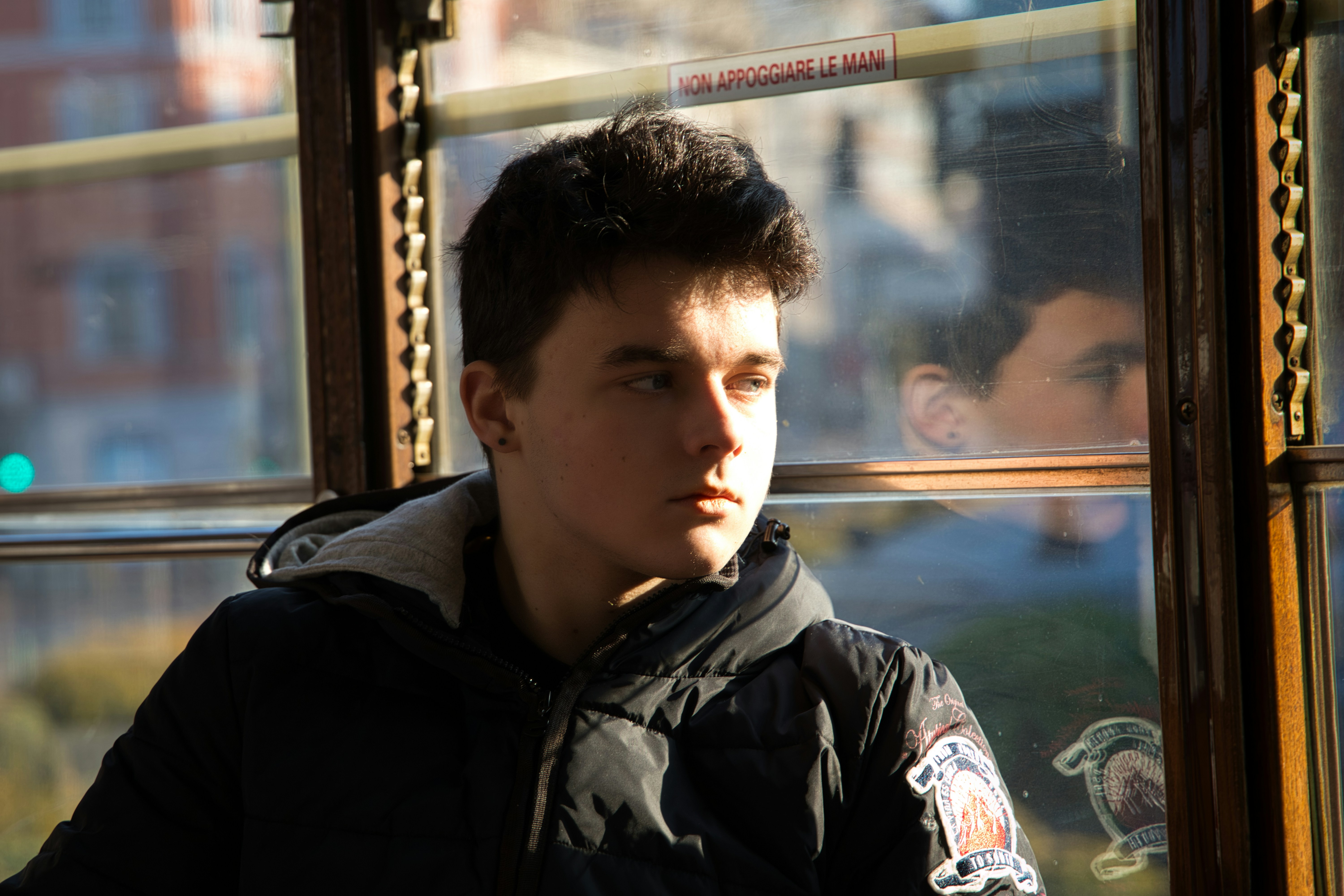 Focused man in dark suit staring pensively at a glass window, reflecting light